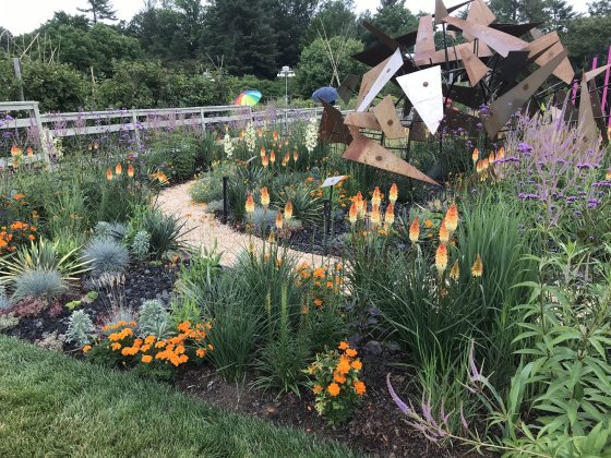An outdoor garden with a large geometric sculpture in the center and orange flowers planted at the base.