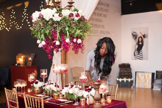A person arranging flowers on a ruby and gold decorated table. 