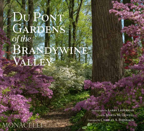 The cover off the Du Pont Gardens of the Brandywine Valley Book features a serene forest image of a walking path through a forest of green trees and pink-blooming shrubs