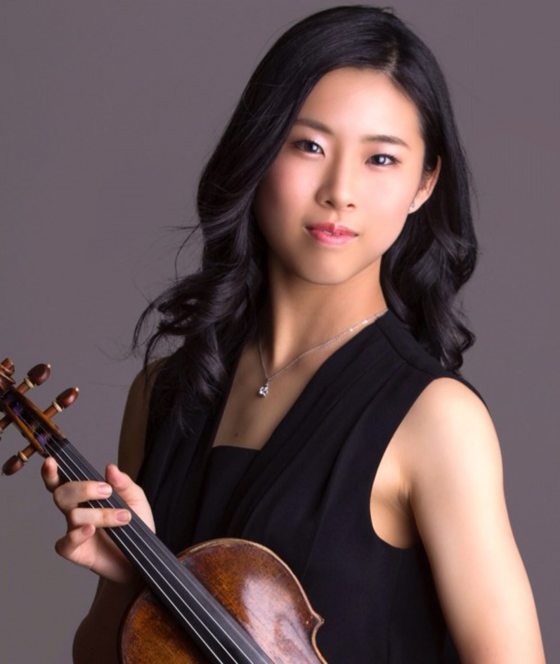 Portrait of a person with long black hair, and dressed in black, holding a violin.
