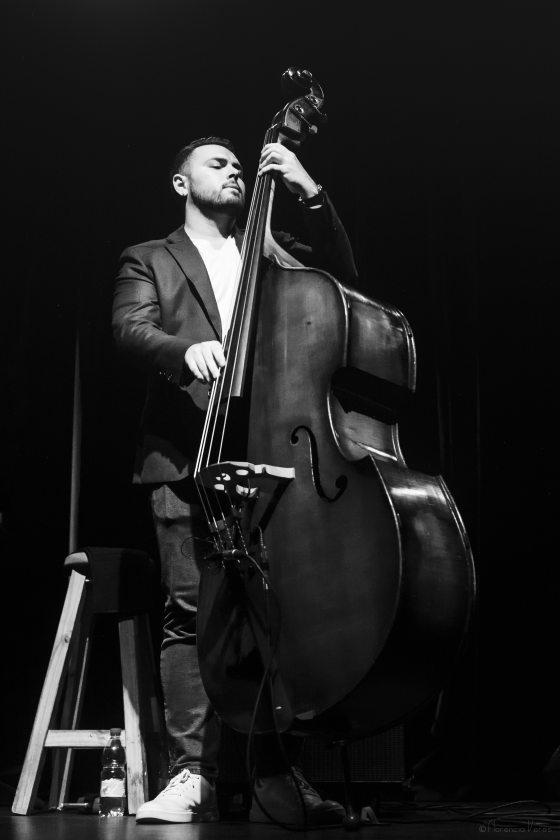 Black and white portrait of a musician standing, eyes closed, playing a bass.