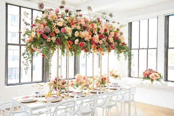 A canopy of flowers in pinks and peach over a white table. 