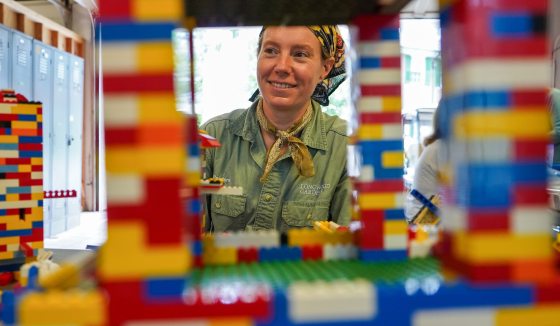 A person smiling through a hole in a birdhouse constructed of legos.