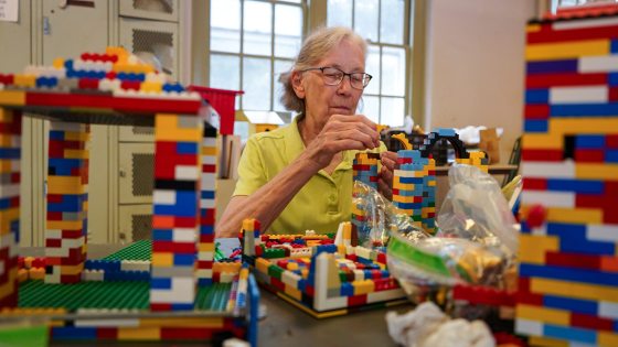 A person in a green shirt with reading glasses putting together legos at a table.