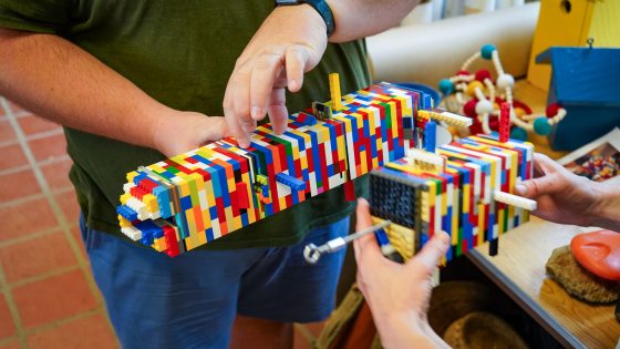 Two people working to bind a bird house made of legos.