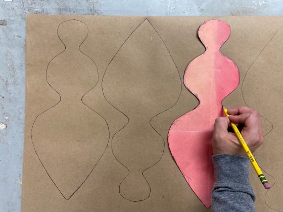 A person's hand tracing a pink shape onto brown paper.