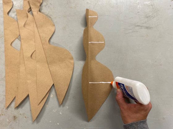 A persons hand placing lines of white glue on a brown paper cutout.