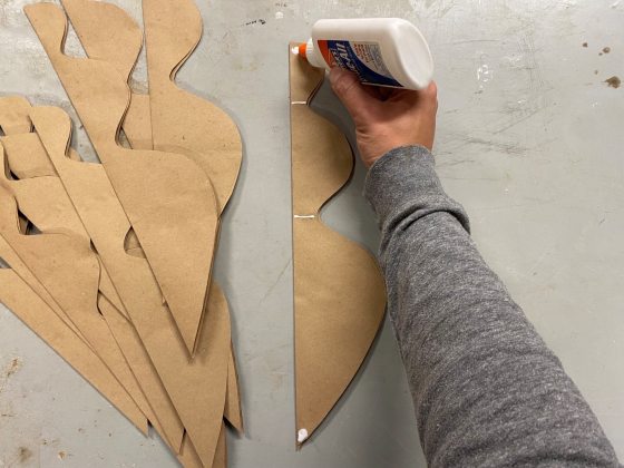 A person gluing brown paper ornament cutouts together.