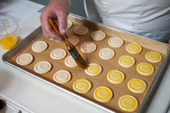 A person applying an egg wash to circles of pastry dough.