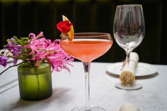 A peach colored cocktail resting on a table with white linen and small pink flowers.