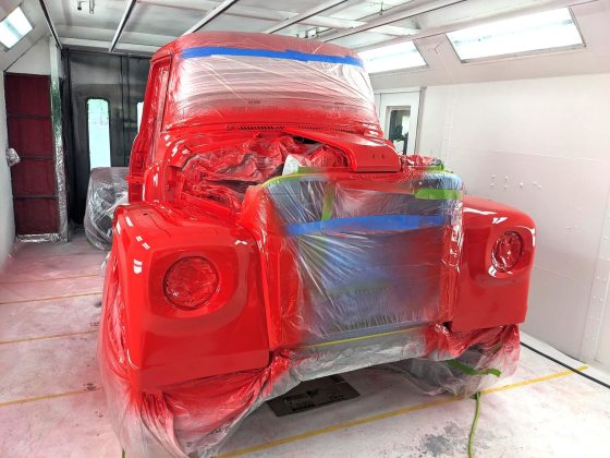 A truck frame in the process of being painted bright red. 