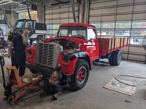 A vintage red pickup truck being restored in a mechanic shop.