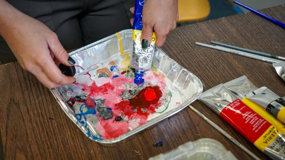 A paint tray with pink, red, and white paint being stirred.