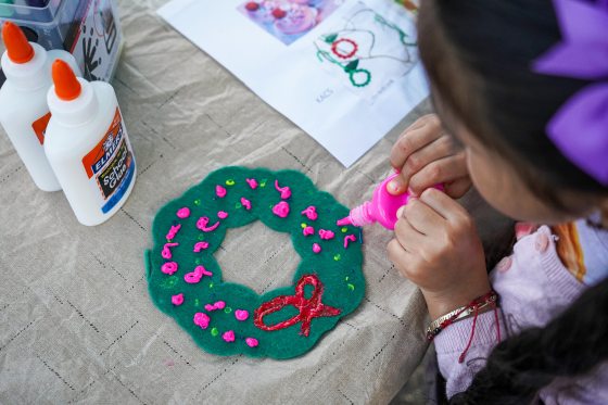 A young child decorating a felt wreath with pink paint. 
