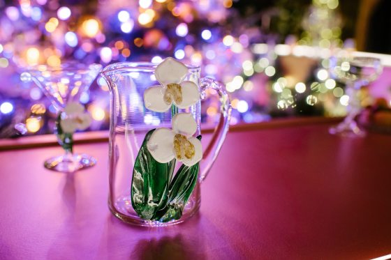 A glass pitcher with blown glass white flowers on it sitting atop a bar.