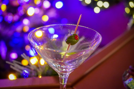 An empty martini glass with a glass olive on a toothpick resting in the glass. 