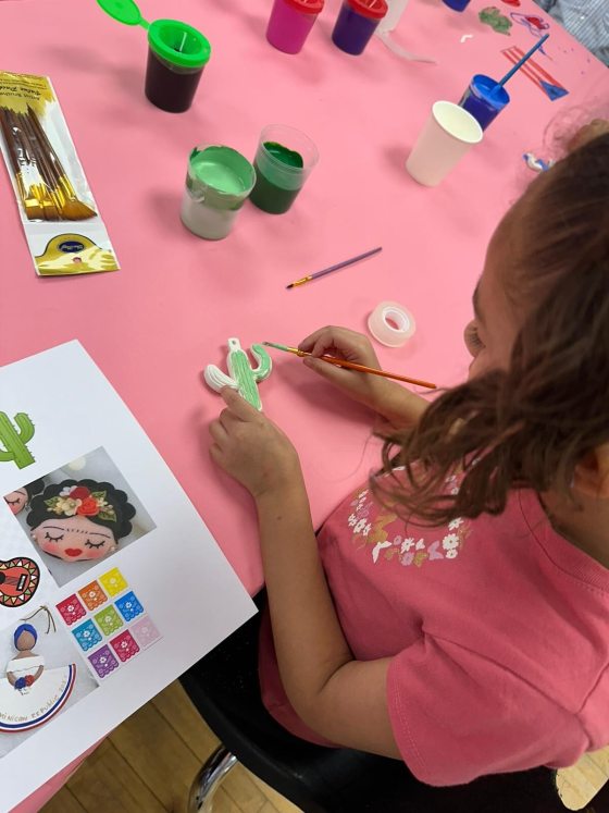 A young child decorating a clay cactus with green paint. 