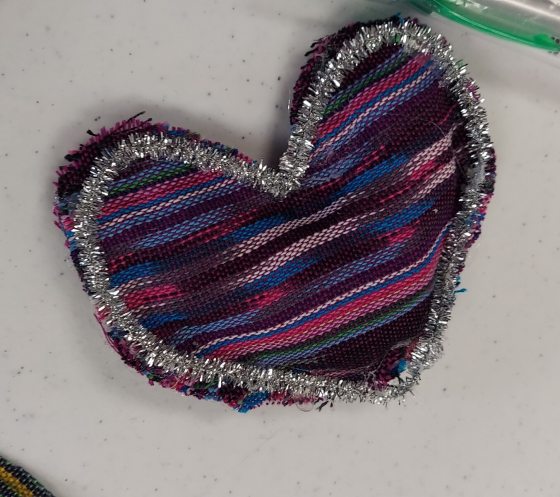 A heart made from pink, black, and purple fabric and outlined with a silver pipe cleaner.