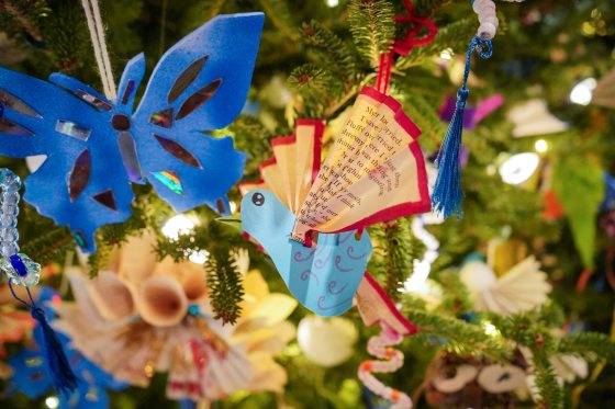 A close of of a butterfly and a bird ornament made of book pages hanging on a Christmas tree. 
