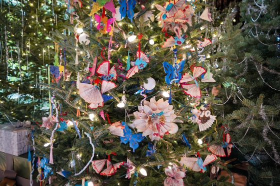 A Christmas tree decorated with ornaments made by young children featuring book pages in different shapes.