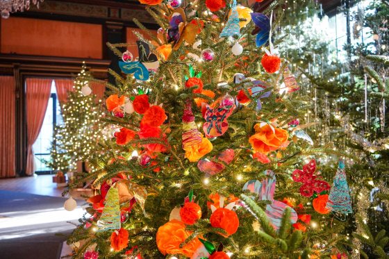 A Christmas tree decorated with ornaments made by young children with a pink, orange, and yellow palatte.