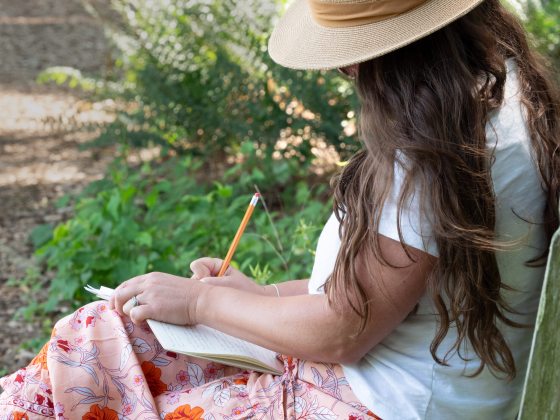 A person sitting outdoors writing in a notebook.