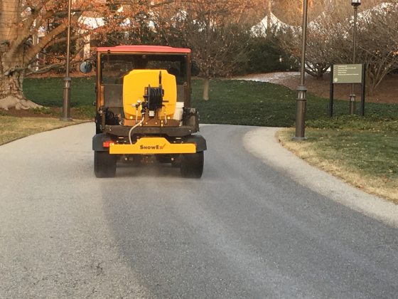 A large yellow vehicle that is spraying brine on paved paths.