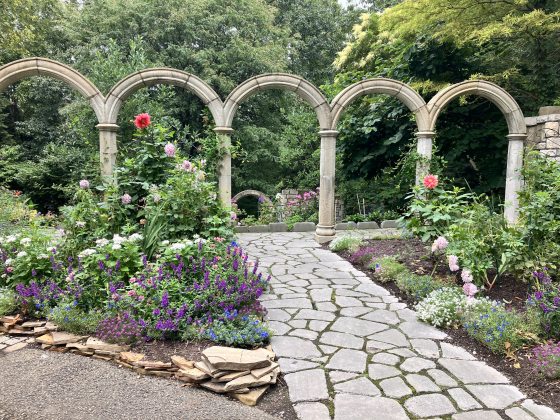 Five arches in an outdoor garden with stone pathways.