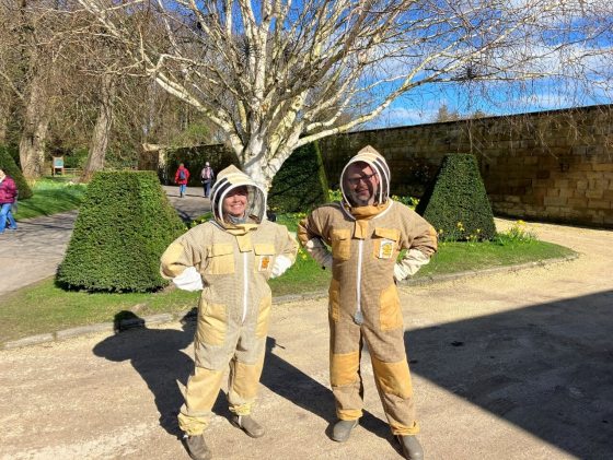 Two people posing for the camera in bee hive protective gear. 