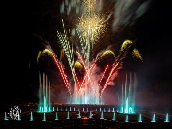Red, white, and blue fireworks over a series of fountains. 