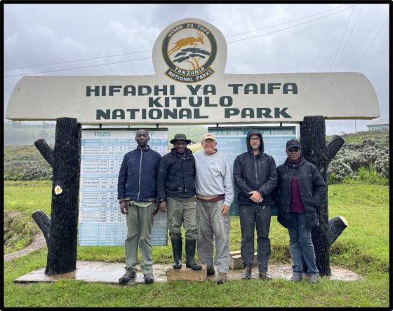 Five men in jackets and hats stand in front of a sign for Hifadhi Ya Taifa Kitulo National Park.