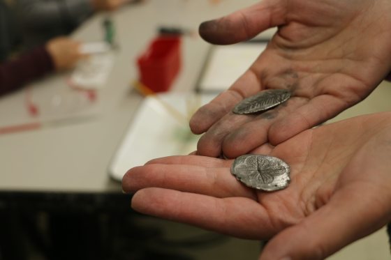 A person hands holding a metal charm with floral imprints.