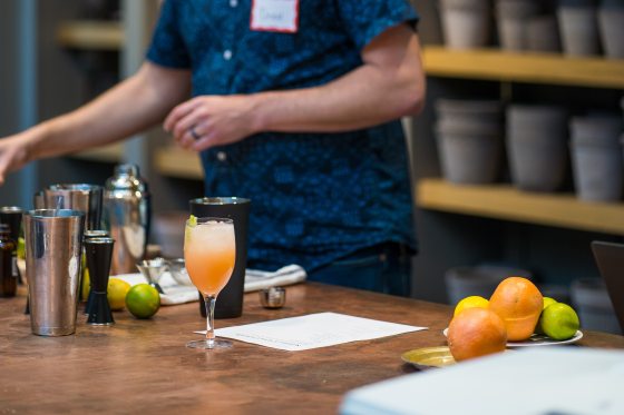 A person behind a wood table creating mixed drinks with citrus.