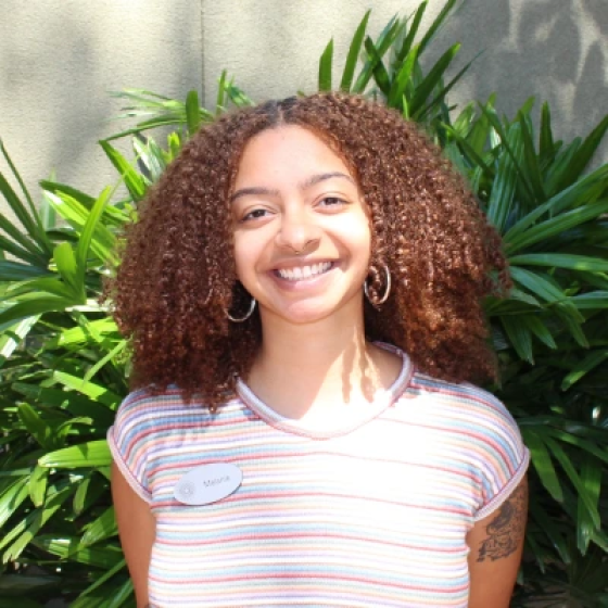 Portrait of smiling person with thick curly light brown hair parted down the middle, wearing a blue and red and white-striped short-sleeved top.