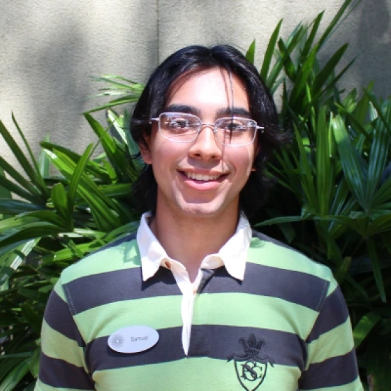 Portrait of smiling person with ear-length black hair, wearing glasses and a collar shirt with large black and lime green stripes.