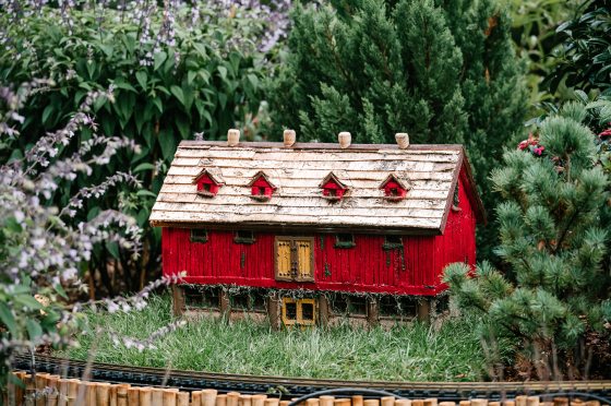 A model of a red barn sitting inside an outdoor model train display.