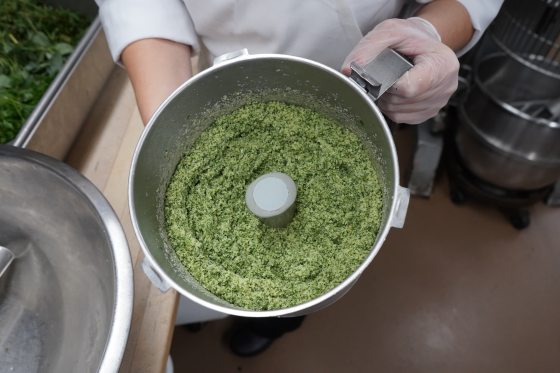 A person holding a bowl of a green herbed paste.