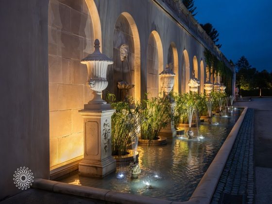 An evening shot of a white stone wall with fountains in front.