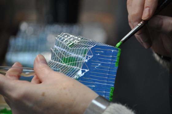 A person using green paint, painting a Christmas ornament.