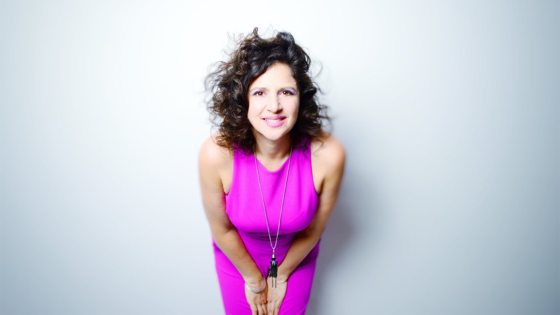 A person with short brown wavy hair, in a bright pink dress, smiling at the camera.