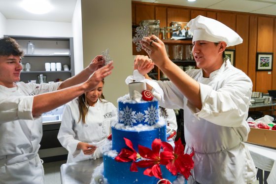Three people in chef uniforms decorating a blue holiday cake.