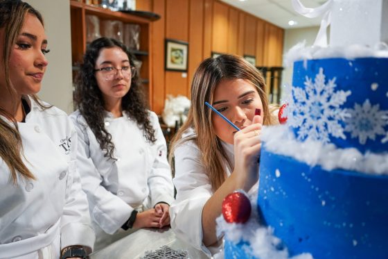 Three people in chef uniforms decorating a blue holiday cake.