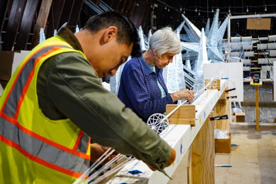 People bent over a white bar, fastening together geometric shapes and straight white poles.