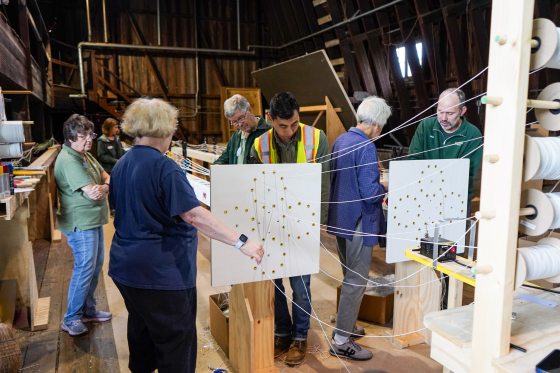 A group of people creating geometric patterns out of white string.
