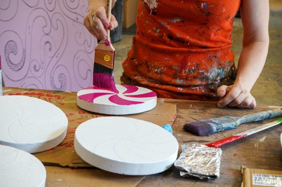 A person painting red swirls onto a large, faux peppermint candy.