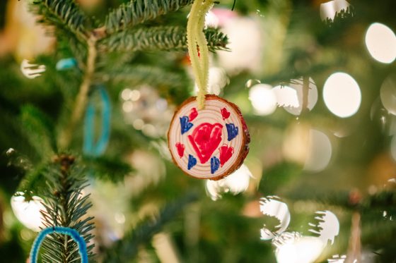 An ornament featuring hearts in red and blue, hanging on a Christmas tree.