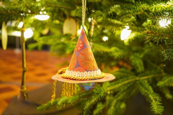 A small witches hat made out of craft paper hanging on a Christmas tree.