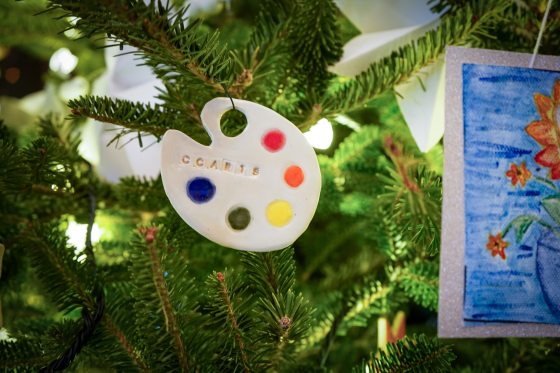 A small painter's pallette made out of clay hanging on a Christmas tree.
