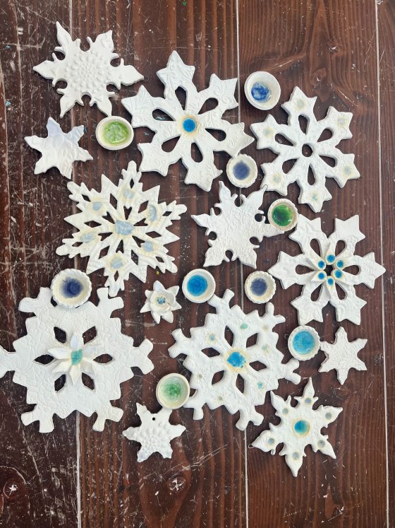 Clay cutouts of snowflakes on a dark wood table.