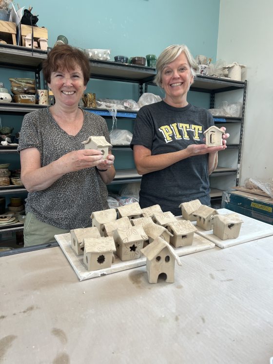 Two people holding small clay birdhouses, smiling at the camera.